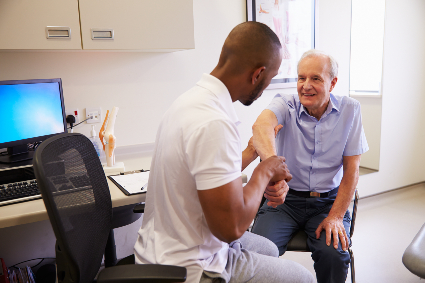 Senior Male Patient Working With Physiotherapist In Hospital